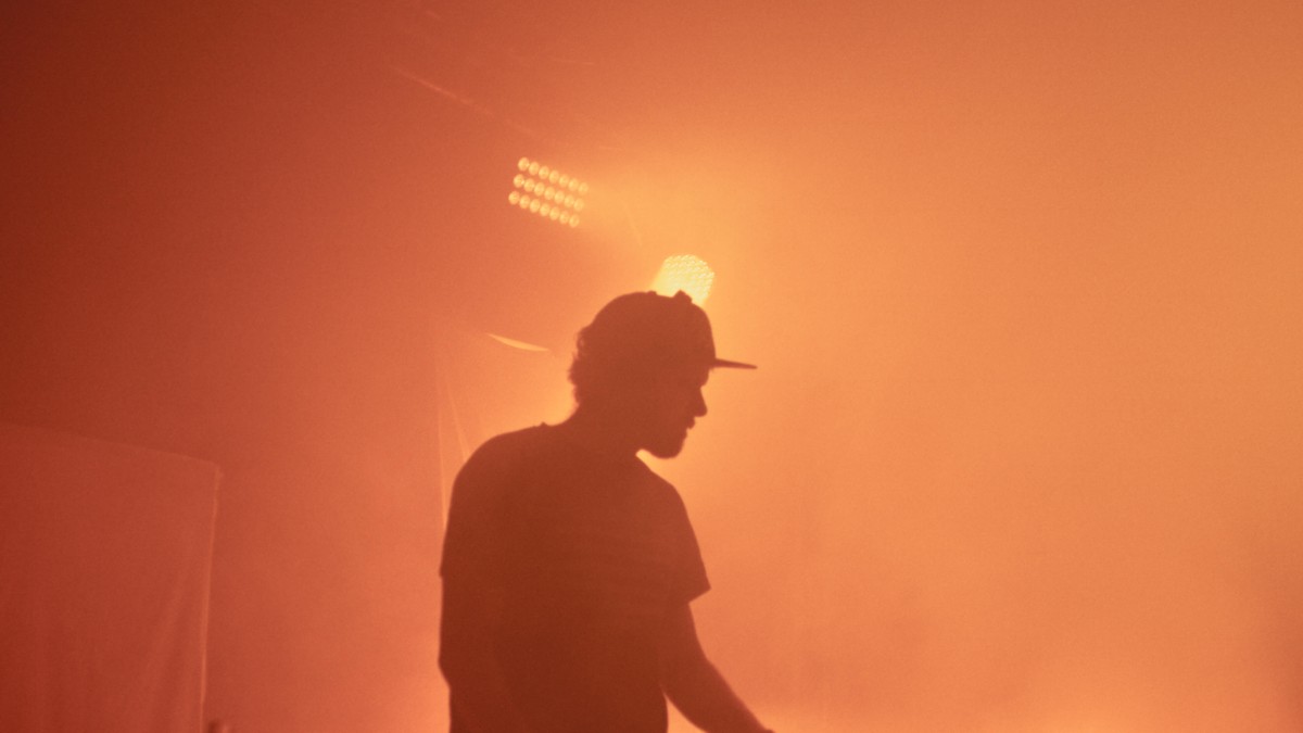 Ein DJ im Gegenlicht als Silhouette, der ganze Raum in orangem Nebel