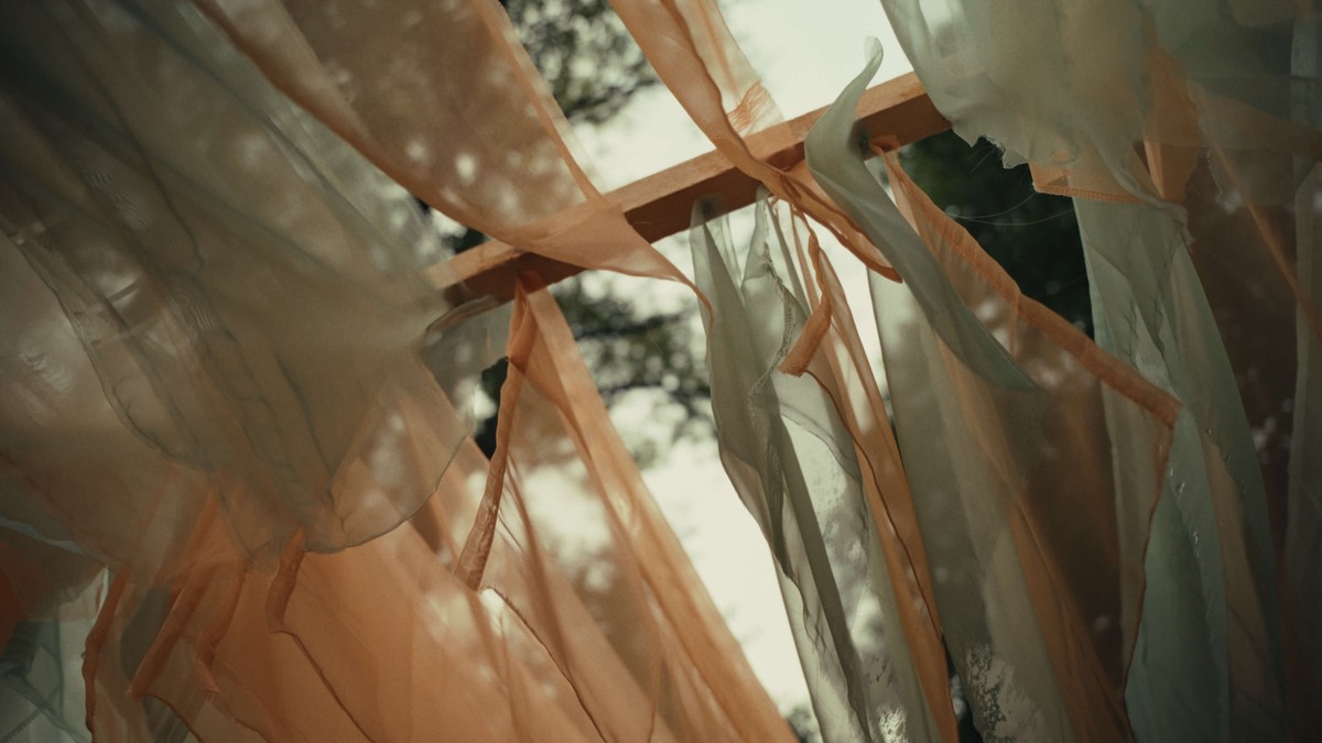 Von unten fotografierte Stoffbahnen in Apricot und Mintgrün, die als Festivaldekoration zwischen Bäumen hängen